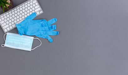 Back to work concept during the coronavirus pandemic with face mask and and gloves on top of computer keyboard