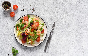 Mix salad with tomatoes and grilled shrimps with sauce and clematis on the kitchen table. View from above. Concrete food background.