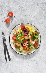 Mix salad with tomatoes and grilled shrimps with sauce and clematis on the kitchen table. View from above. Concrete food background.