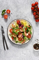 Mix salad with tomatoes and grilled shrimps with sauce and clematis on the kitchen table. View from above. Concrete food background.