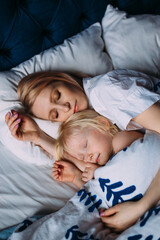 Cute little girl sleeping with mother in bed. Interior. Concept care