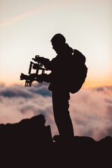 Videographer man shooting footage using dlsr camera mounted on gimbal stabilizer equipment. Video production crew for movie, cinema. Silhouette of professional filmmaker filming outdoor. - 426196923