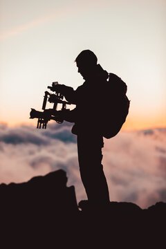 Videographer man shooting footage using dlsr camera mounted on gimbal stabilizer equipment. Video production crew for movie, cinema. Silhouette of professional filmmaker filming outdoor.