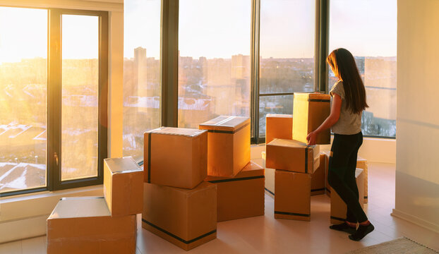 Moving Into New Home Movers Pick-up Service. Woman Ready To Move From Apartment With Belongings Packed In Many Cardboard Boxes Packages For Shipping.