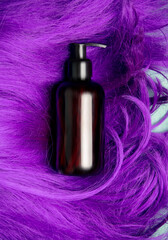 Obraz premium Dark bottle of shampoo on purple hair, top view