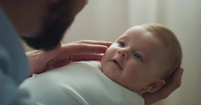 Cinematic close up shot of young neo father is playing with his newborn baby in a nursery in a morning. Concept of children, baby, parenthood, childhood, life, love, fatherhood, family.