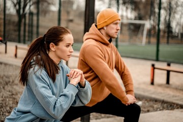 Young couple in sports outfit doing morning workout outdoors. Young man and woman stretching they muscle before running on street sports ground. Staying fit and healthy concept.