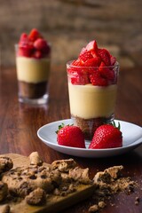 A glass filled with crunched cookies and vanilla pudding and garnished with strawberries