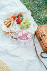 Fototapeta na wymiar Spring picnic in nature. A glass of pink champagne with sakura flowers, a wicker bag, a hat, Italian. Wine. Spring.