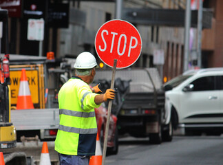 Male construction road worker holding a stop sign and directing traffic on the street. Traffic...