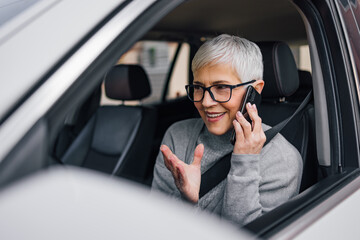 Close-up image of a smiling senior female driver talking on smart phone.