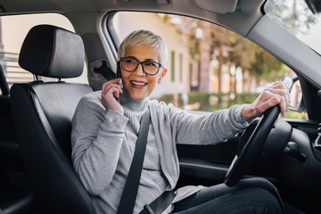 Portrait of a beautiful senior woman having a phone call while driving a car.