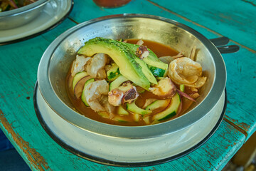 Camarones en aguachile servidos en plato de metal sobre un fondo azul verdoso