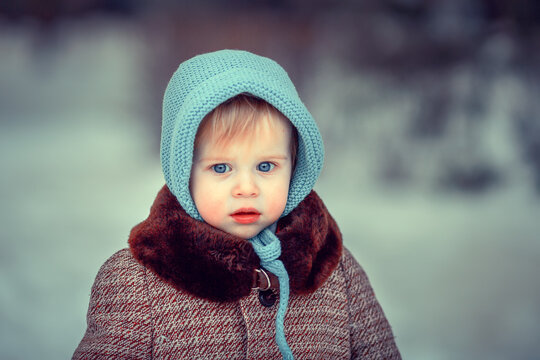Winter portrait of cute sad little girl with blue eyes and in blue bonnet. Image with selective focus and toning