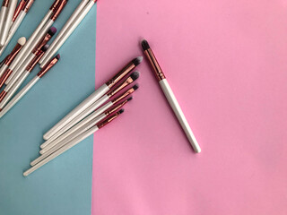 Different makeup brushes and broken eye shadow on pastel pink background. Flat lay, top view