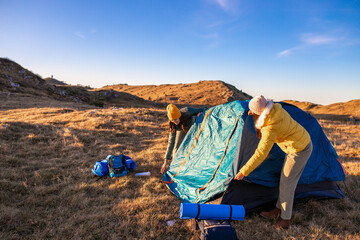 Women building a tent in the mountains, preparing for a camping night.	