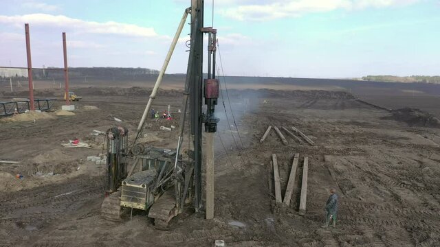Excavation at a construction site, diesel pile driving machine with rumble and smoke drives piles deep into the ground to ensure the strength of the foundation of the future structure