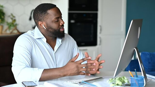 Online conversation. Attractive friendly successful young african american businessman, broker, or lawyer works remotely at computer, talking to employee or client by online conference, discuss ideas