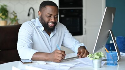 Confident successful african american male student or freelancer, working or study remotely at home uses computer, listening online lecture via video conference, smiling friendly, takes notes