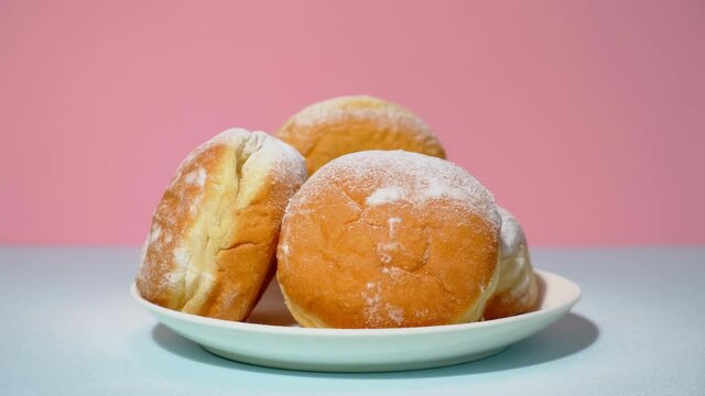 Classic European donuts sprinkled with powdered sugar. Plate with powdered doughnuts on pink background. Sweet traditional german, polish pastries.