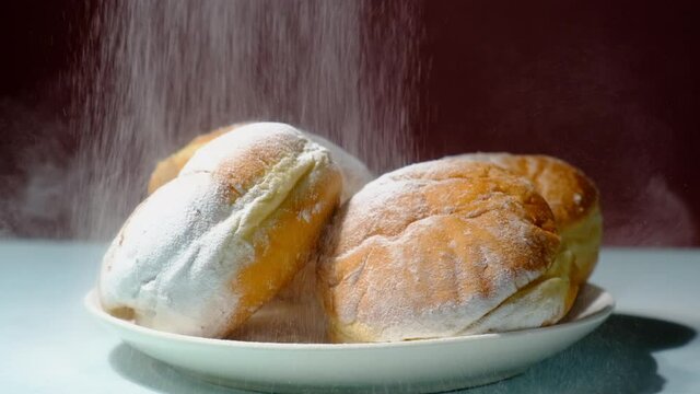 Classic European donuts sprinkled with powdered sugar. Plate with powdered doughnuts on dark background. Sweet traditional german, polish pastries. Slow motion.