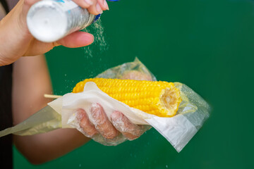 person holding corn. Boiled ripe corn cob with salt close-up photo with a human hand take one. A woman's hand holds a freshly prepared yellow corn sprinkled with salt. Seasonal street trading