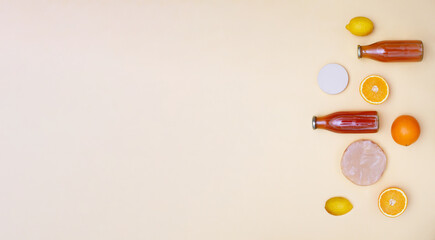 Horizontal banner with two bottles of kombucha tea, scoby and fruits for additional flavors on yellow pastel background. Orange, lemon, apple. Healthy fermented drink. Flatlay mockup, copy space