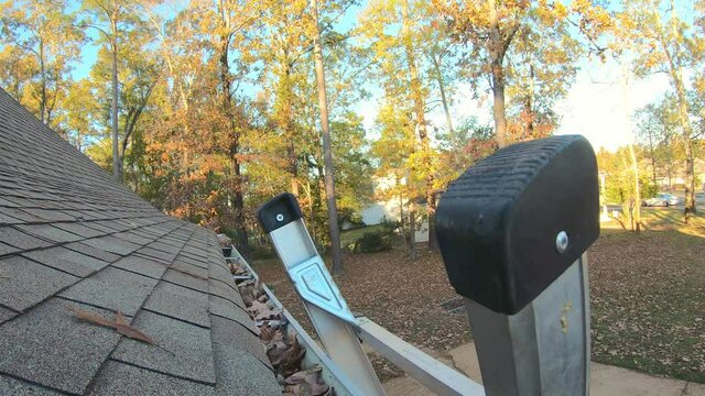Man climbs ladder and cleans leaves from gutter.