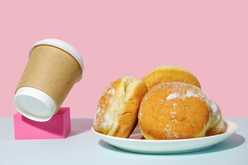 Donuts sprinkled with powdered sugar and coffee container on trendy minimal coloured background. Takeaway food and fastfood concept.