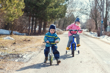 Children ride a bicycle and a runbike along the village road