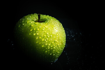 Green apple with drops of water on a black background