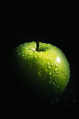 Green apple with drops of water on a black background