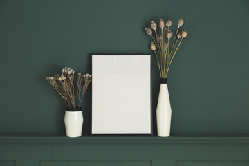 Frame mock up and vase with dried flowers against dark paneled wall.
