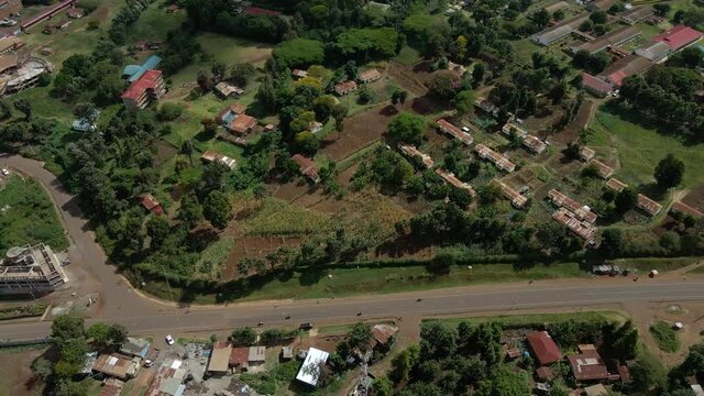 Aerial drone view over cars on village streets and homes with yards and farmlands, in a rural Africa