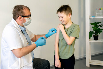 Fototapeta premium A male doctor in a protective mask and with a stethoscope vaccinates a child.