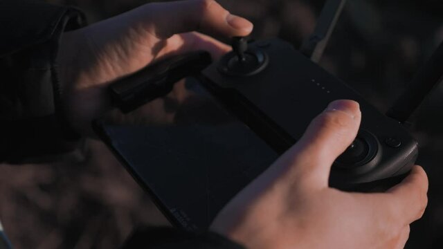 Close-up view of person&rsquo;s hands using a controller with a smart phone mounted to it to operate a drone UAV DJI Mini quad copter with no logo or symbols on equipment slow motion