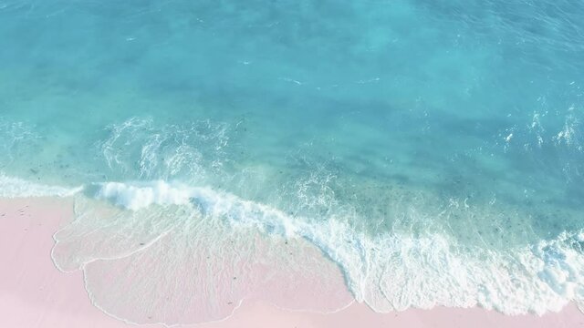 Top-down aerial of ocean waves crashing, foaming on pink sand beach. Nature nobody seascape. Sandy shore of light blue water. Tropical turquoise wavy coastline. Unique tourists landmark on Bahamas