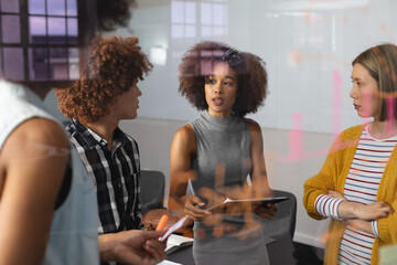 Diverse group of creative colleagues brainstorming in meeting room holding documents taking notes