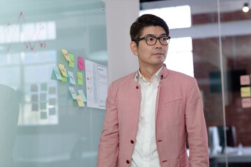 Portrait of stylish asian businessman by glass wall looking away