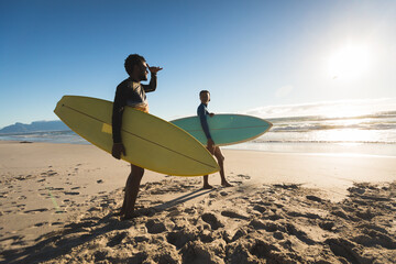 Happy african american couple on the beach carrying surfboards