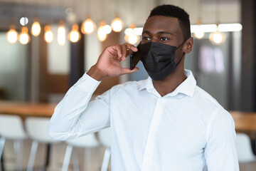 Casual african american businessman wearing face mask talking on smartphone