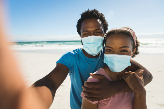 African american couple on beach by the sea wearing masks taking selfie