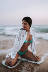 Fototapeta na wymiar Chica guapa feliz en bikini paseando por la playa en traje de baño durante la a puesta de sol en la arena y las rocas