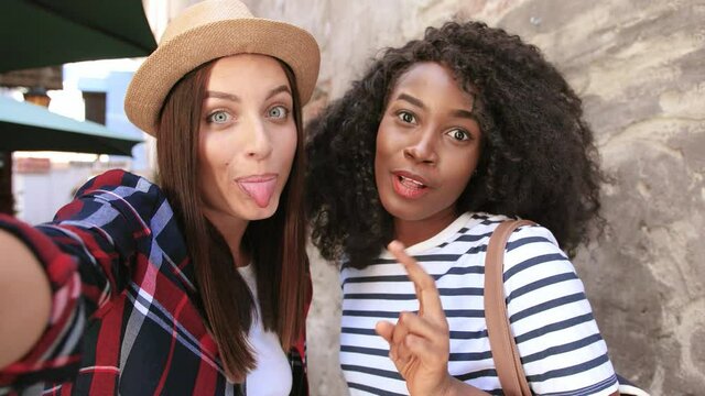 Close up of two cheerful tourist, african american girl with curly hair and caucasian woman in hat posing for selfie. View from camera.