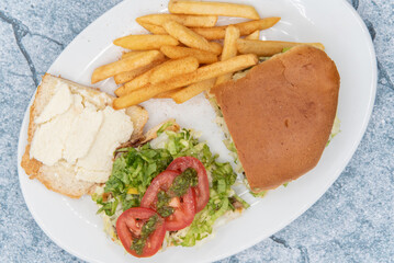 Overhead view of large Churrasquito sandwich lies open with juicy tomato slices on top served with french fries.