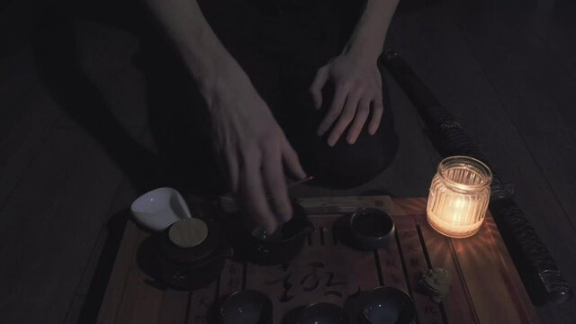 It dark, candle is burning. Man sitting on his knees pours himself a green tea and drinks the drink. Next to man lies a Japanese, samurai katana sword. Concept of martial arts, hobbies and lifestyle