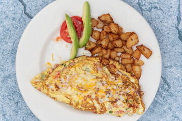Overhead view of omelette cooked to the perfect level of frimness folded and served with cubed breakfast potatoes and sliced avocado.