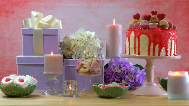 4k Mother's Day or Birthday party table with stack of gifts, cookies, flowers, and showstopper drip cake. Continuous loop cinemagraph with burning candles.