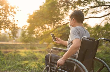 Happy Paralyzed,disabled or handicapped man in hope sitting relax on a wheelchair in nature park.Disabled handicapped man has a hope use smart phone for working,calling and searching for social media