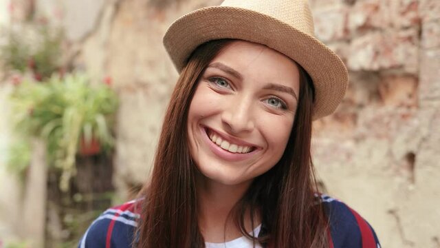 Close up portrait of young tourist girl in hat with beautiful eyes standing on street and looking at camera smiling.